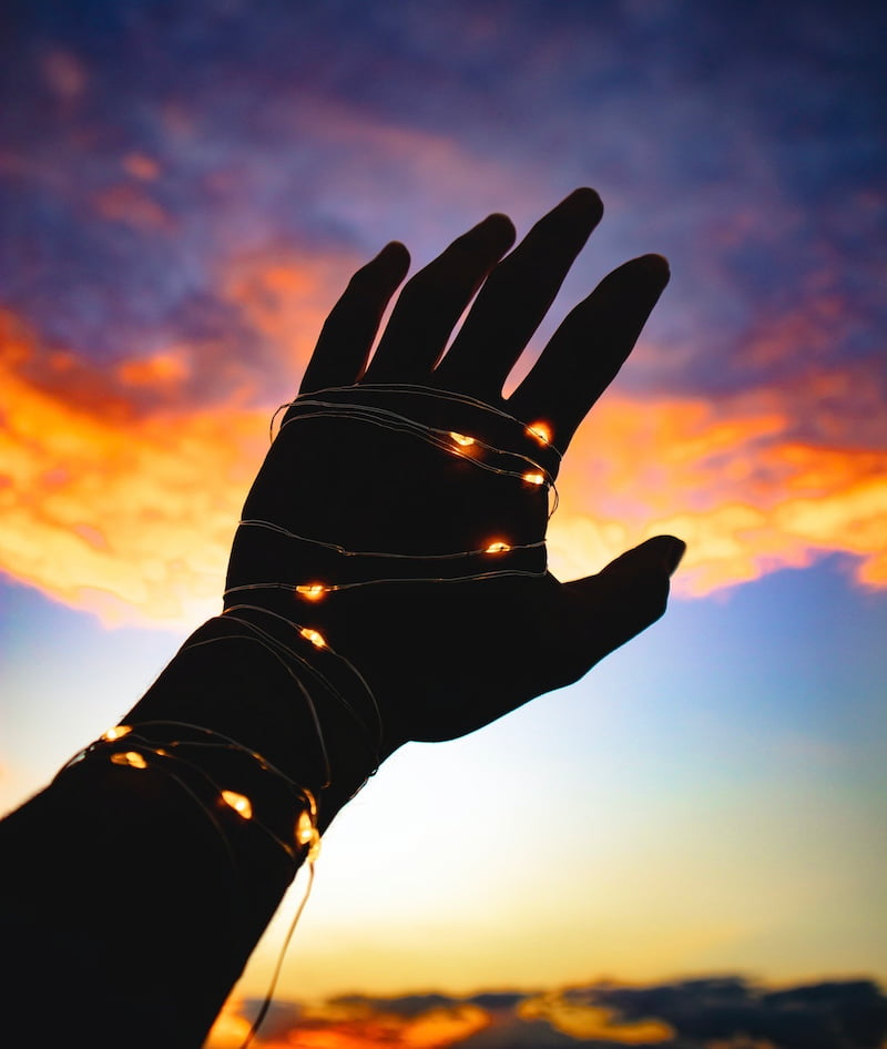 Image of a hand reaching up to the evening sky with fairy lights wrapped tightly around it symbolizing feeling trapped