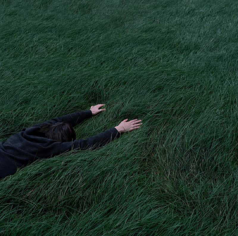 Image of a tired and exhausted person face first in a field of grass symbolic of feeling trapped in life