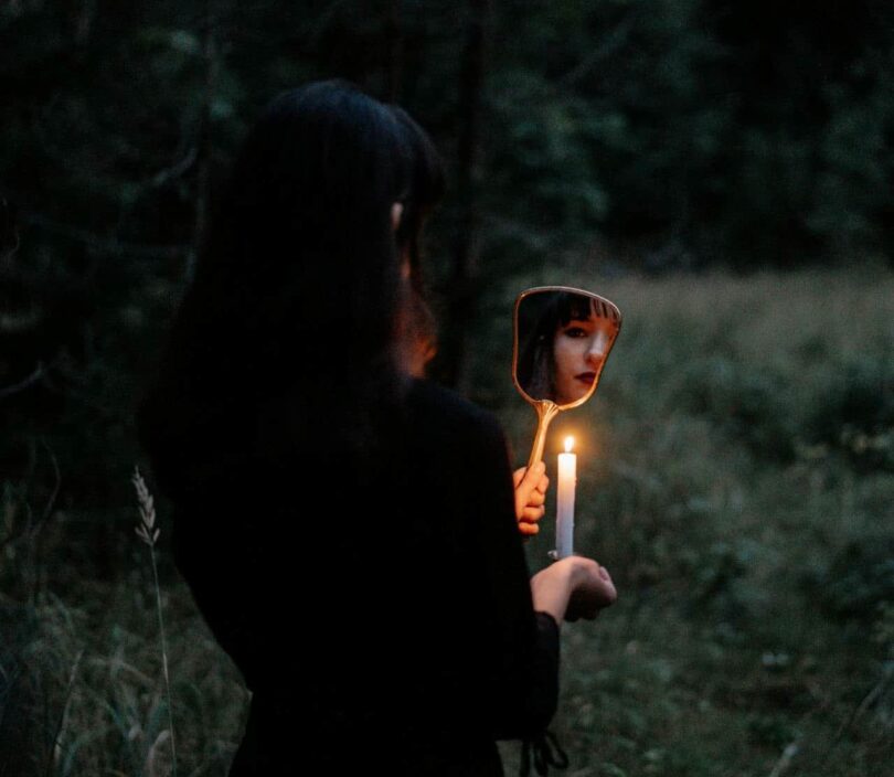 Image of a woman looking into a mirror holding a candle at night symbolic of practicing shadow work